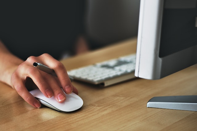 Cropped image of a person's hand holding a pen while using a white computer mouse